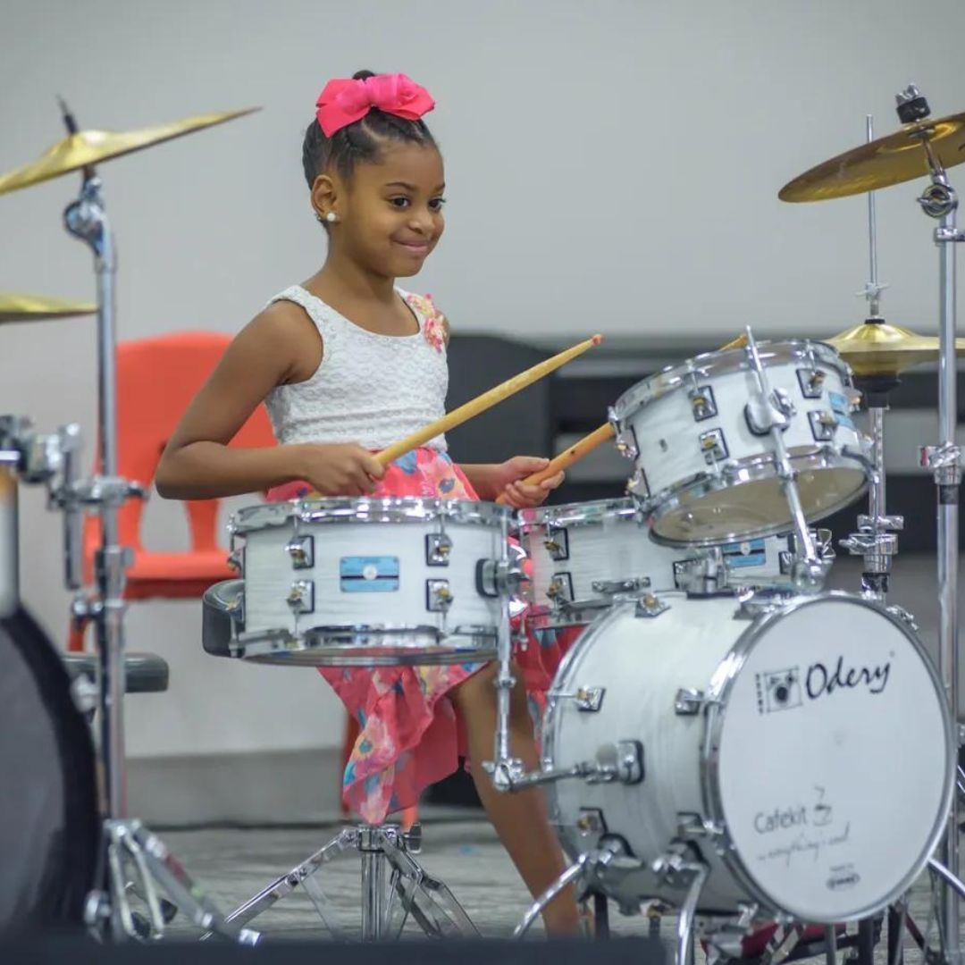 A young girl is sitting at a drum set playing drums.