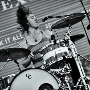 A man is playing drums in front of a microphone in a black and white photo.