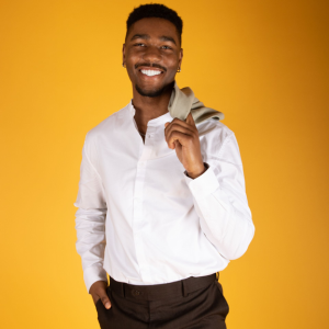 A man in a white shirt and brown pants is holding a tie over his shoulder