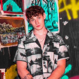 A young man standing in front of a wall with paintings on it