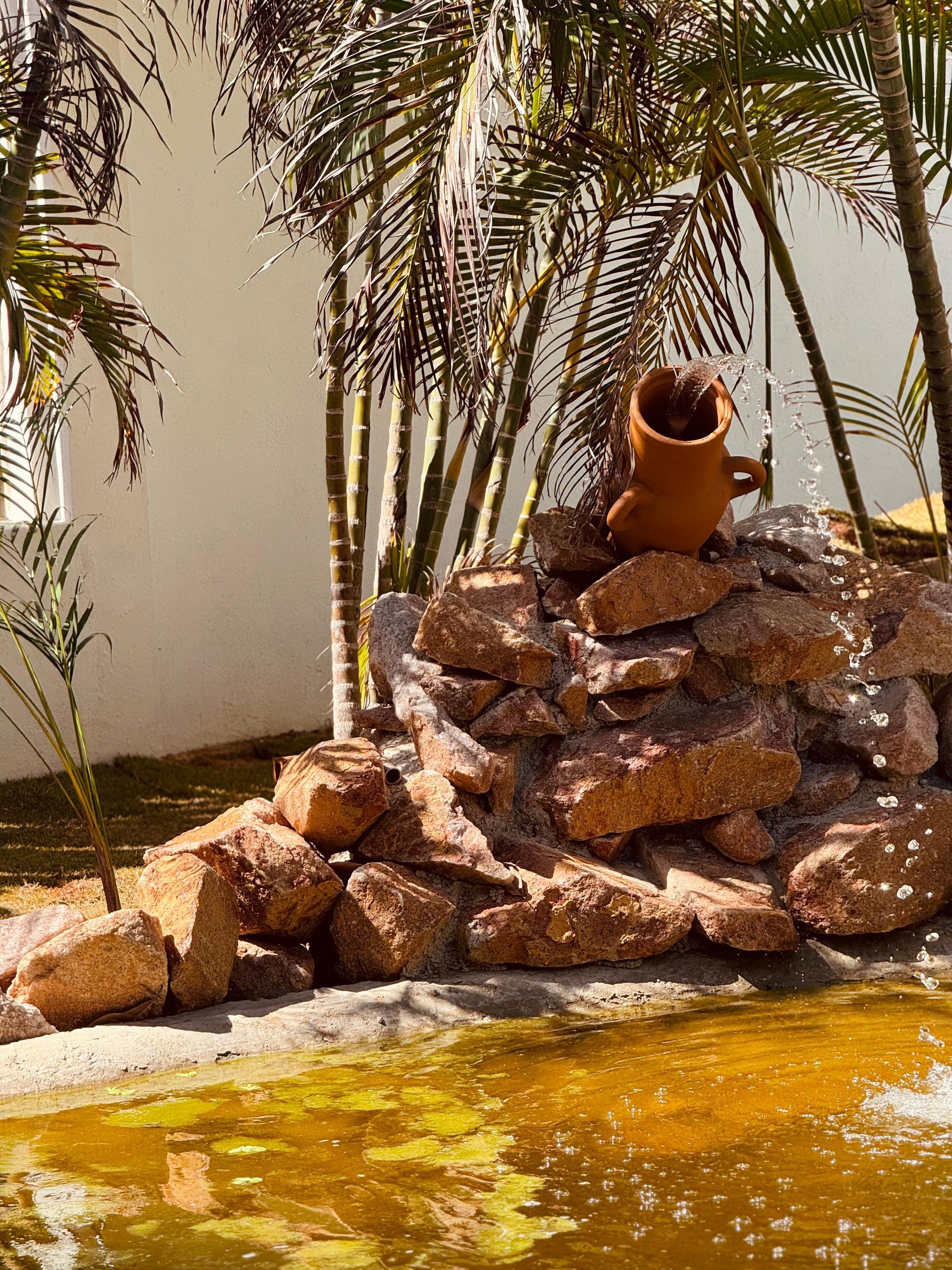 Um lago com uma fonte no meio, cercado por árvores e pedras. - Villa Manzuá