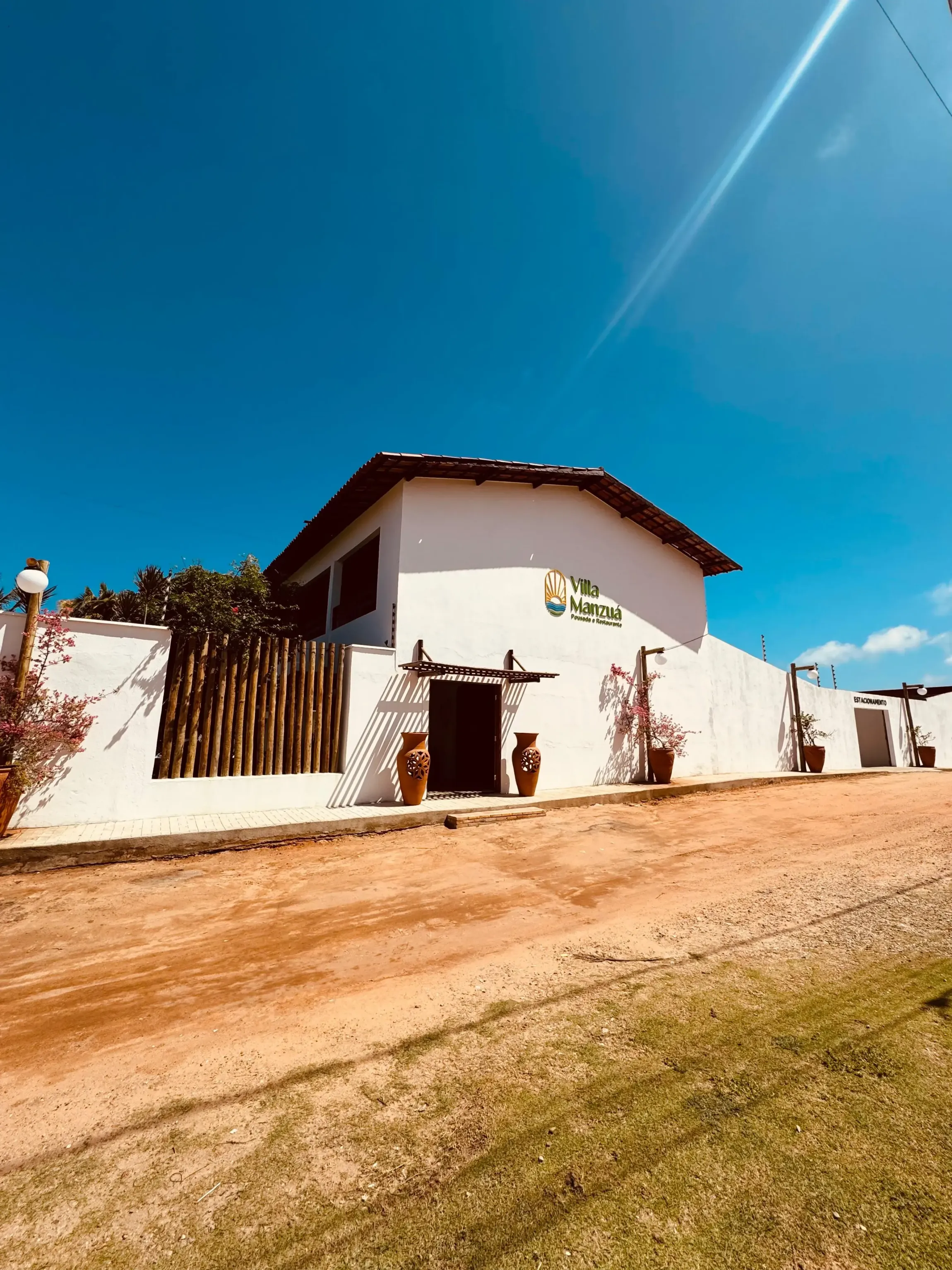 Uma casa branca com uma cerca de madeira e uma estrada de terra na frente. - Villa Manzuá