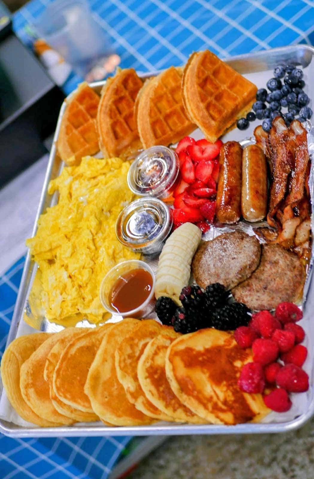 Breakfast platter with waffles, pancakes, eggs, sausage, bacon, berries, and syrup.