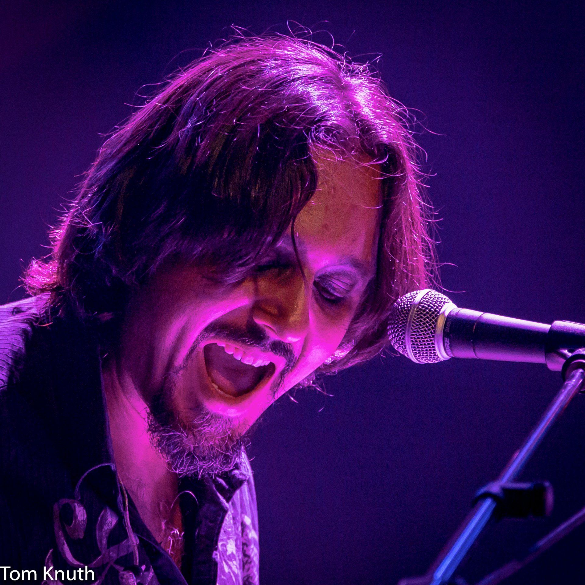 A man singing into a microphone with purple lights behind him