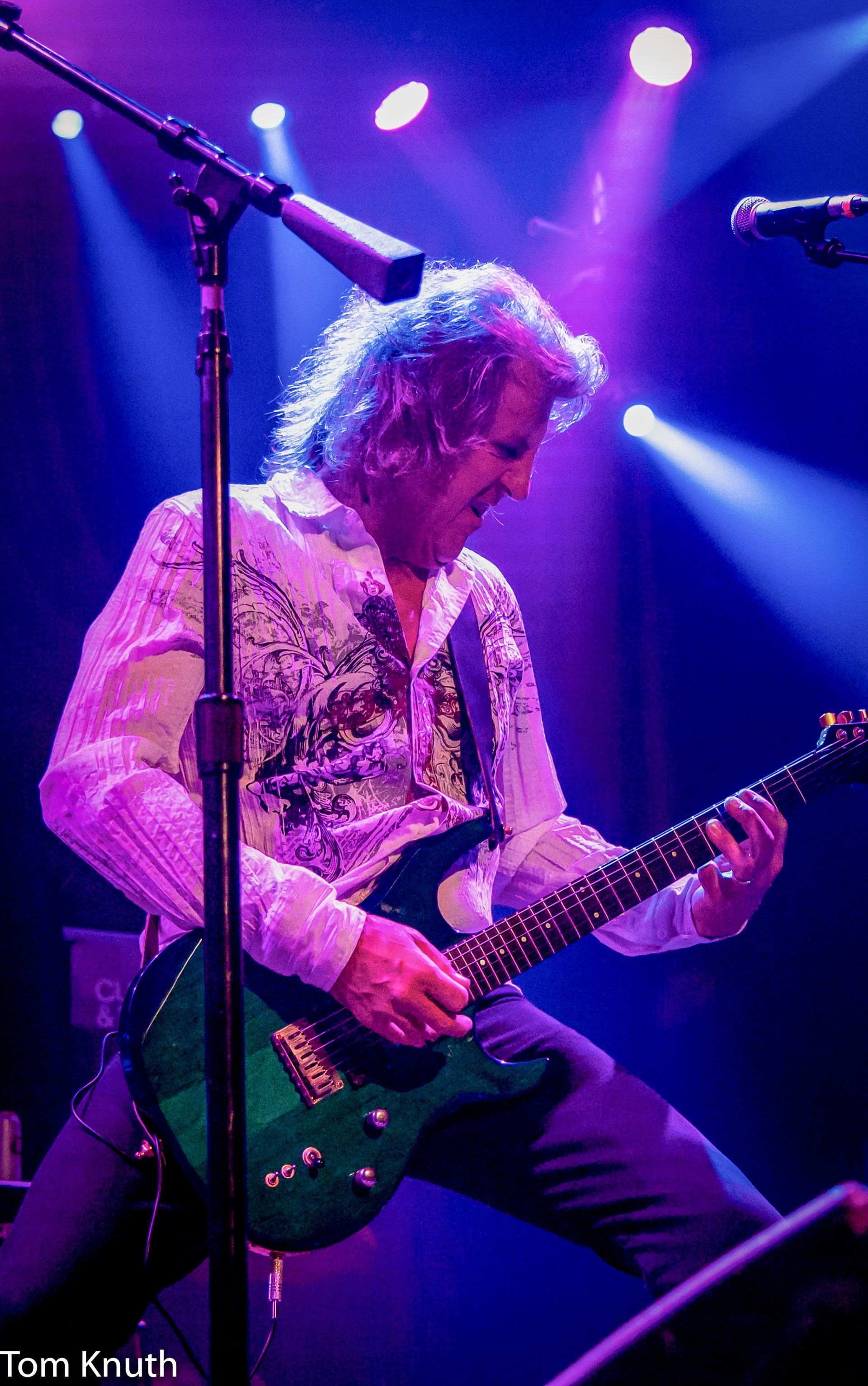 A man is playing a guitar in front of a microphone on a stage.