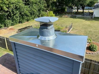 A metal chimney on top of a blue house with a fence in the background.