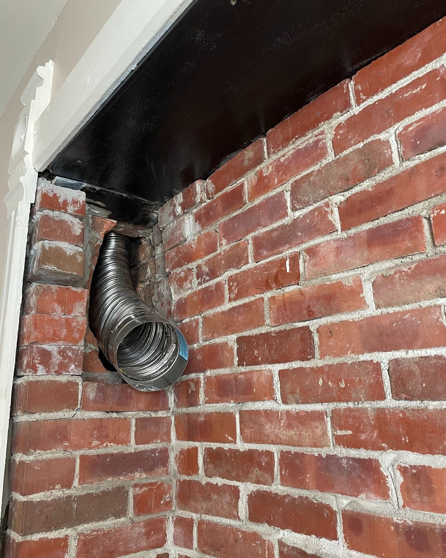 A metal hose is hanging from a brick wall.