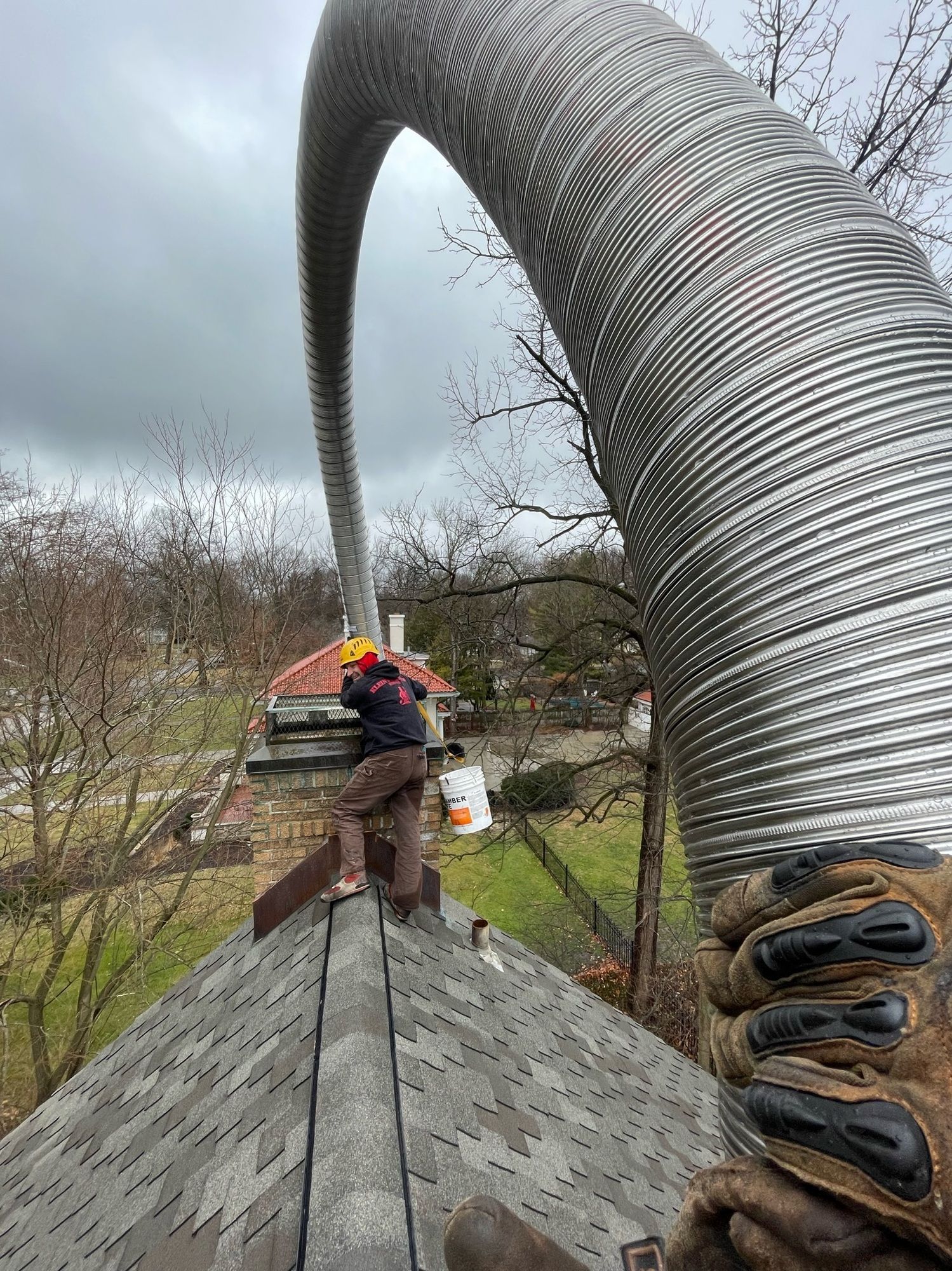 A man is standing on top of a roof with a hose coming out of it.