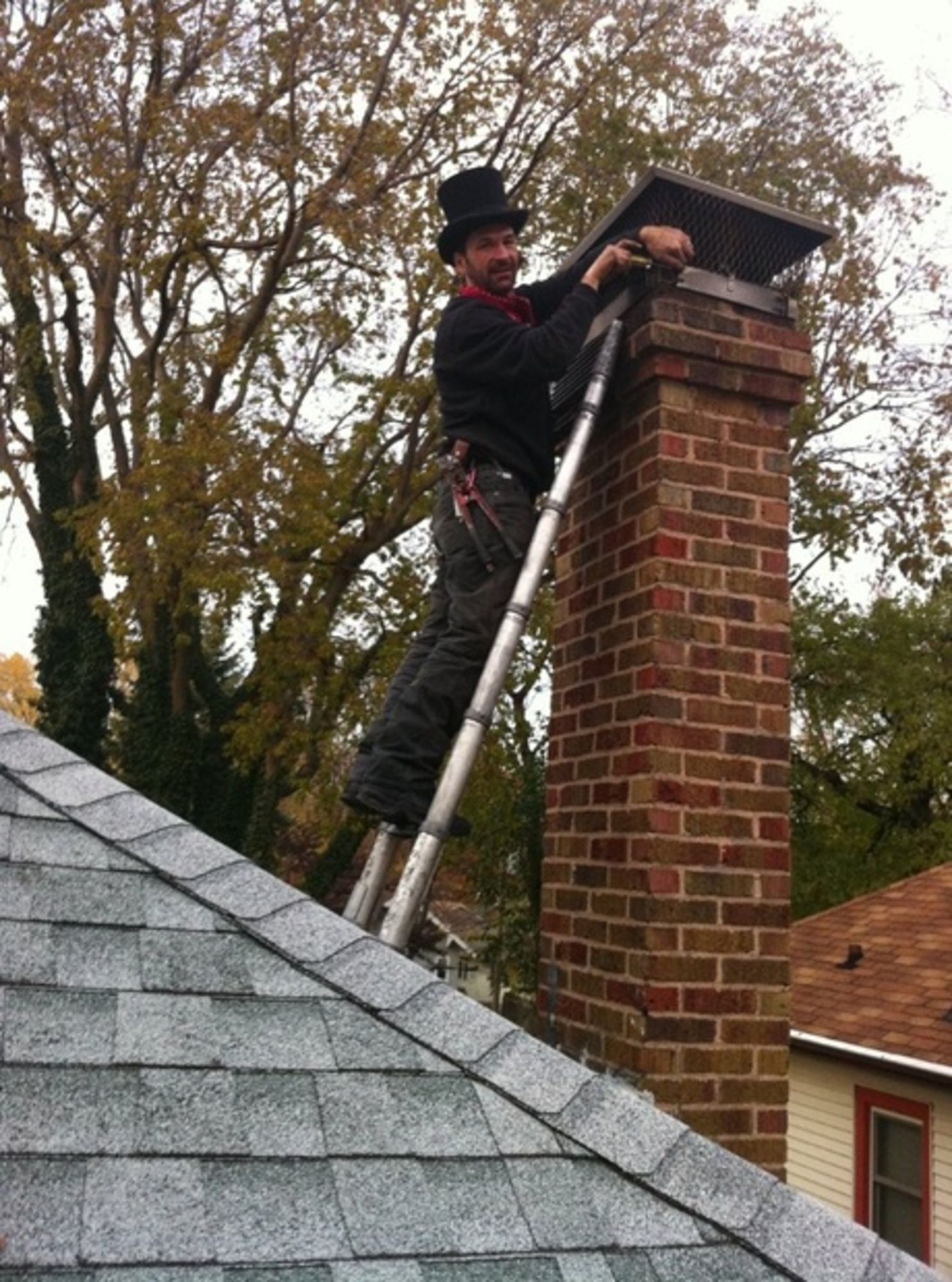 A man is standing on a ladder on top of a brick chimney.