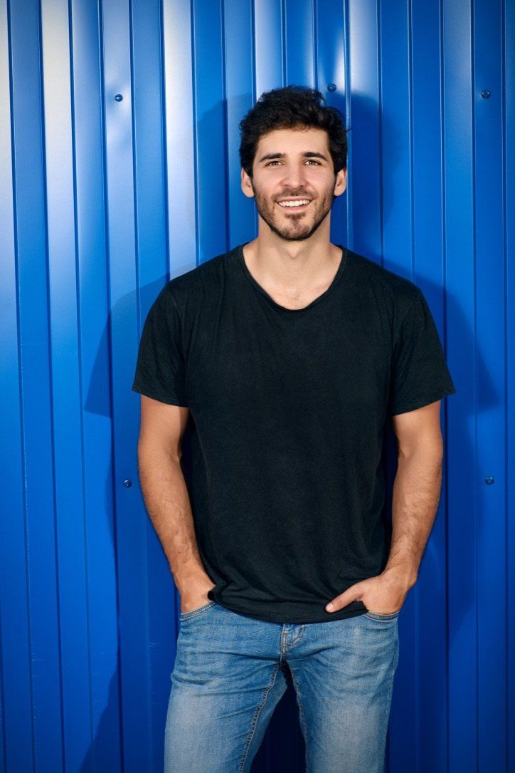 junger Mann mit weißen Zähnen der auf blauem Hintergrund lächelt