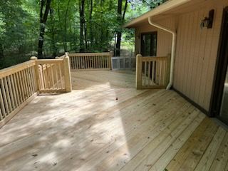 A large wooden deck is sitting outside of a house surrounded by trees.
