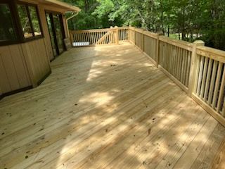 A large wooden deck with a railing in front of a house.