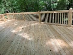 A wooden deck with a wooden railing and trees in the background.