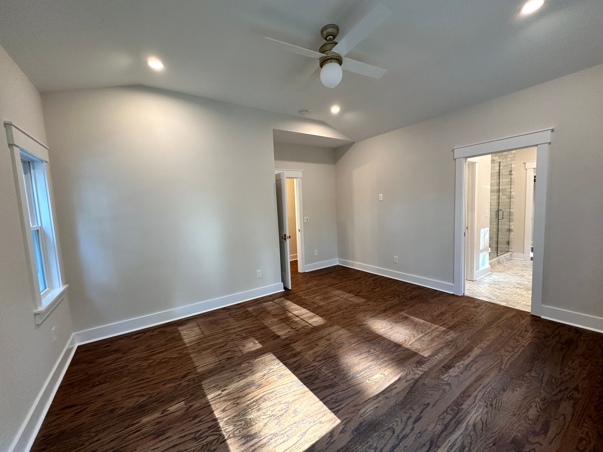 An empty room with hardwood floors and a ceiling fan.