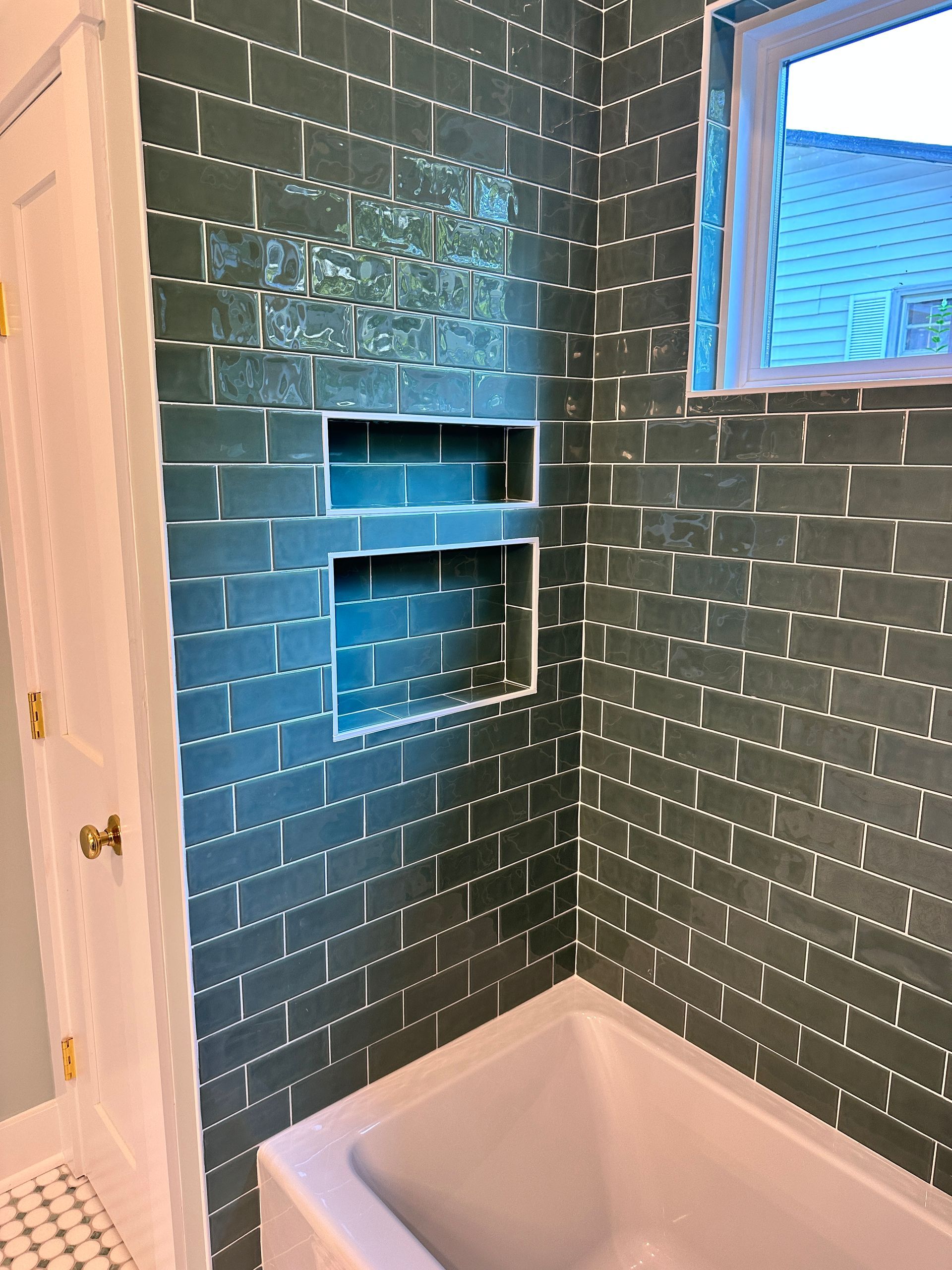 A bathroom with green brick tiles and a bathtub