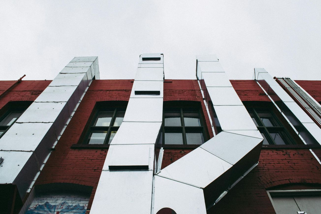 Low-angle view of a red brick building with white vertical metal structures and dark windows