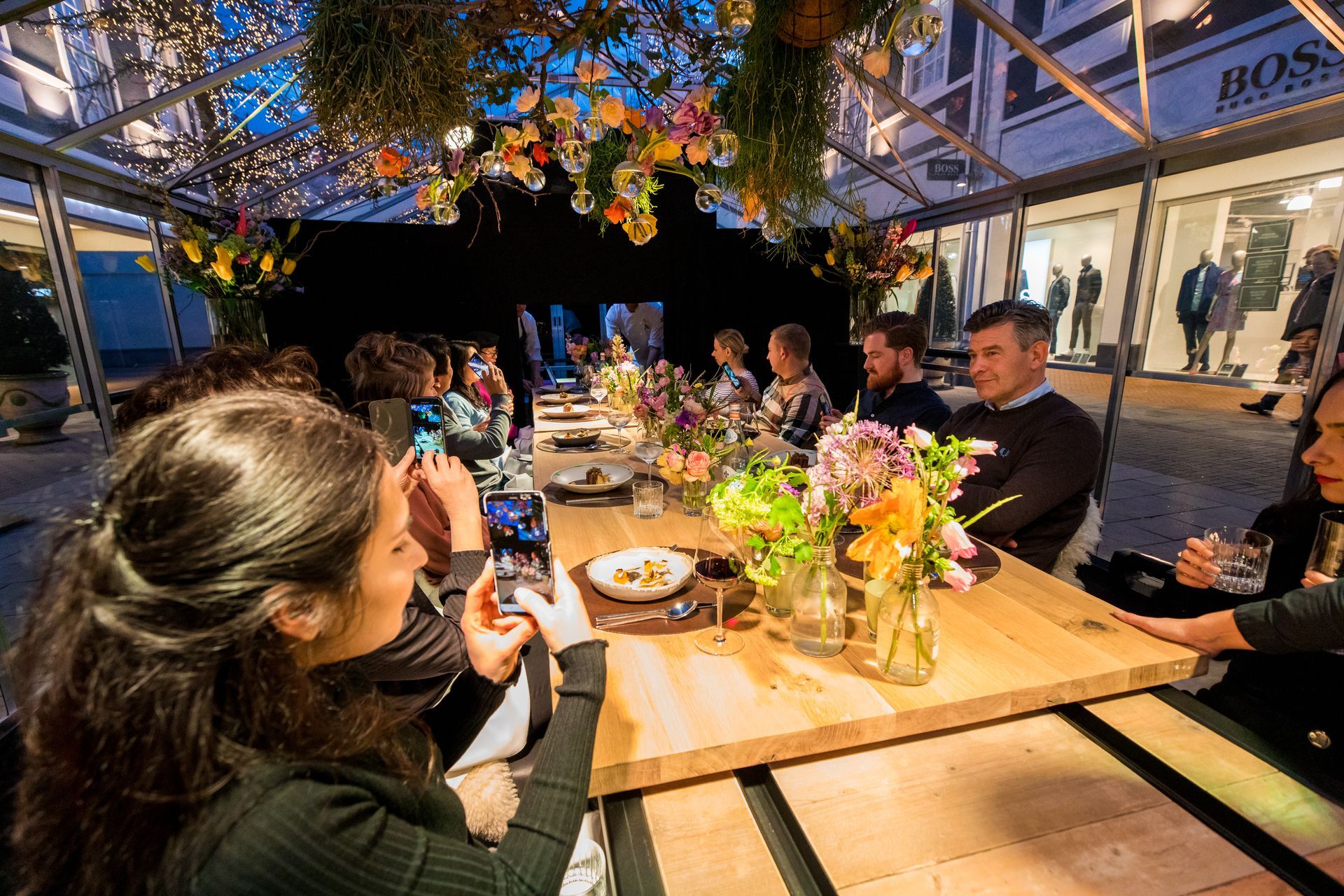 Een groep mensen zit aan een lange tafel met bloemen erop.