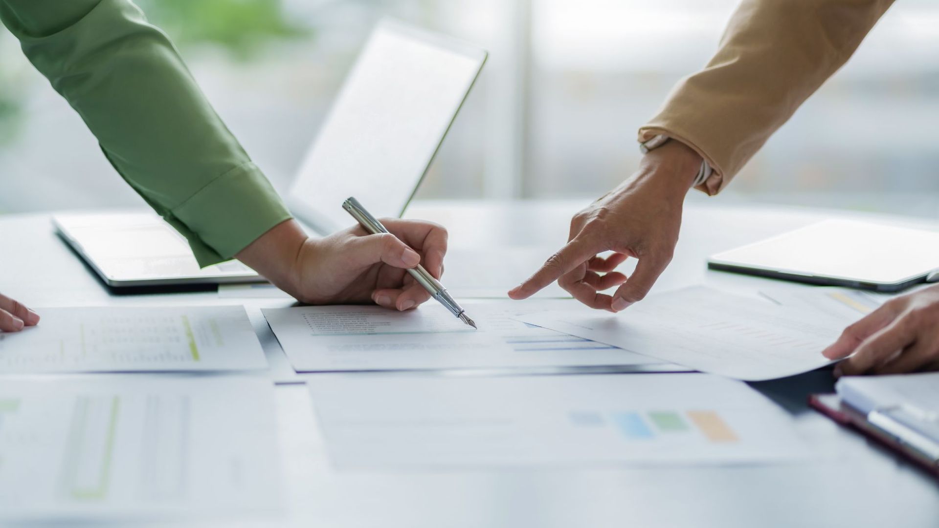 Hands pointing to documents, one writing with a pen, collaborating over paperwork.