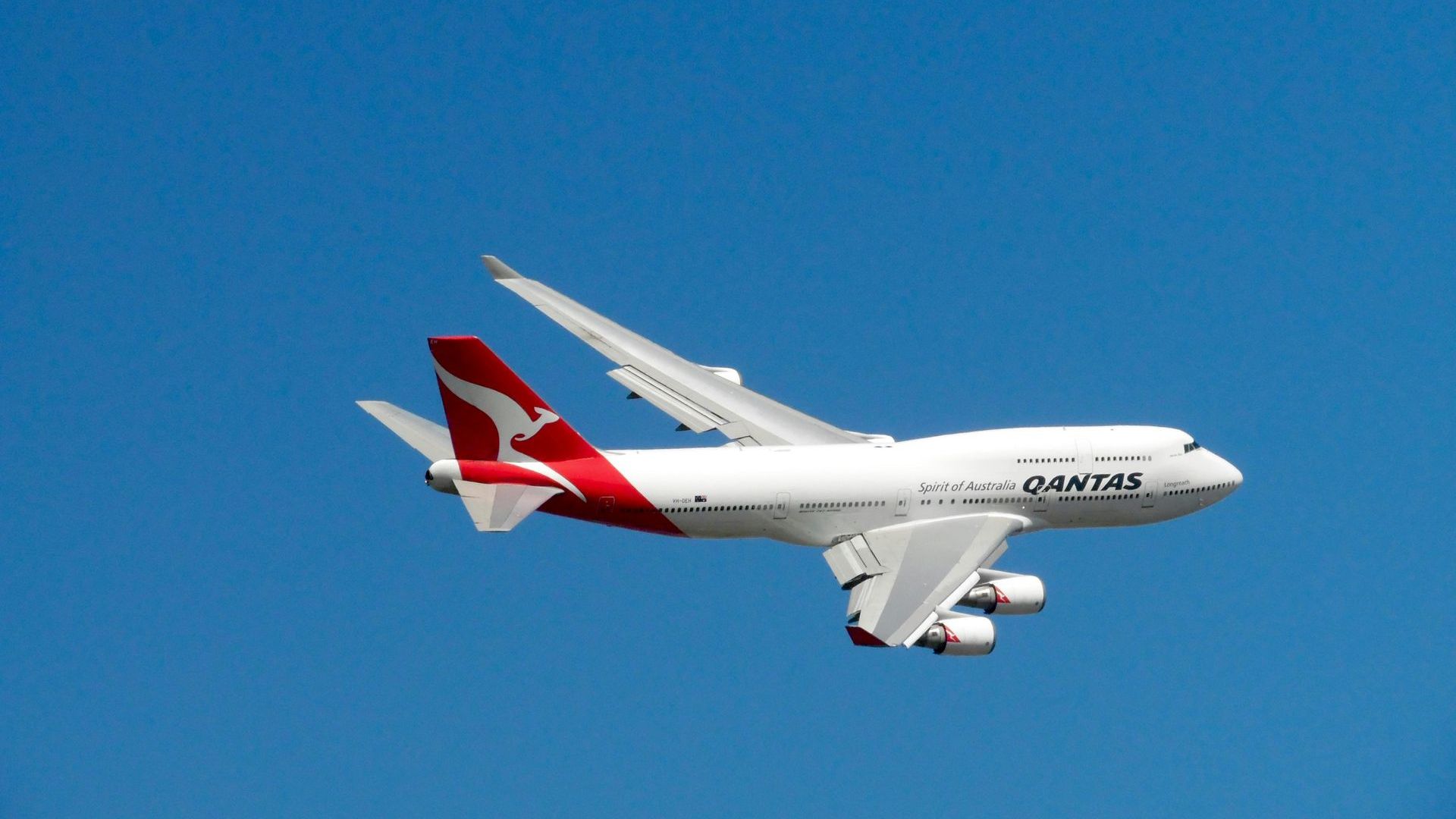 A qantas airplane is flying through a clear blue sky