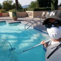 A man wearing a mask and a hat is cleaning a swimming pool.