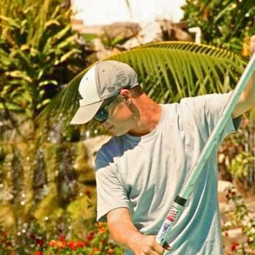 A pool cleaner wearing a baseball cap and sunglasses is holding a pool cleaner.