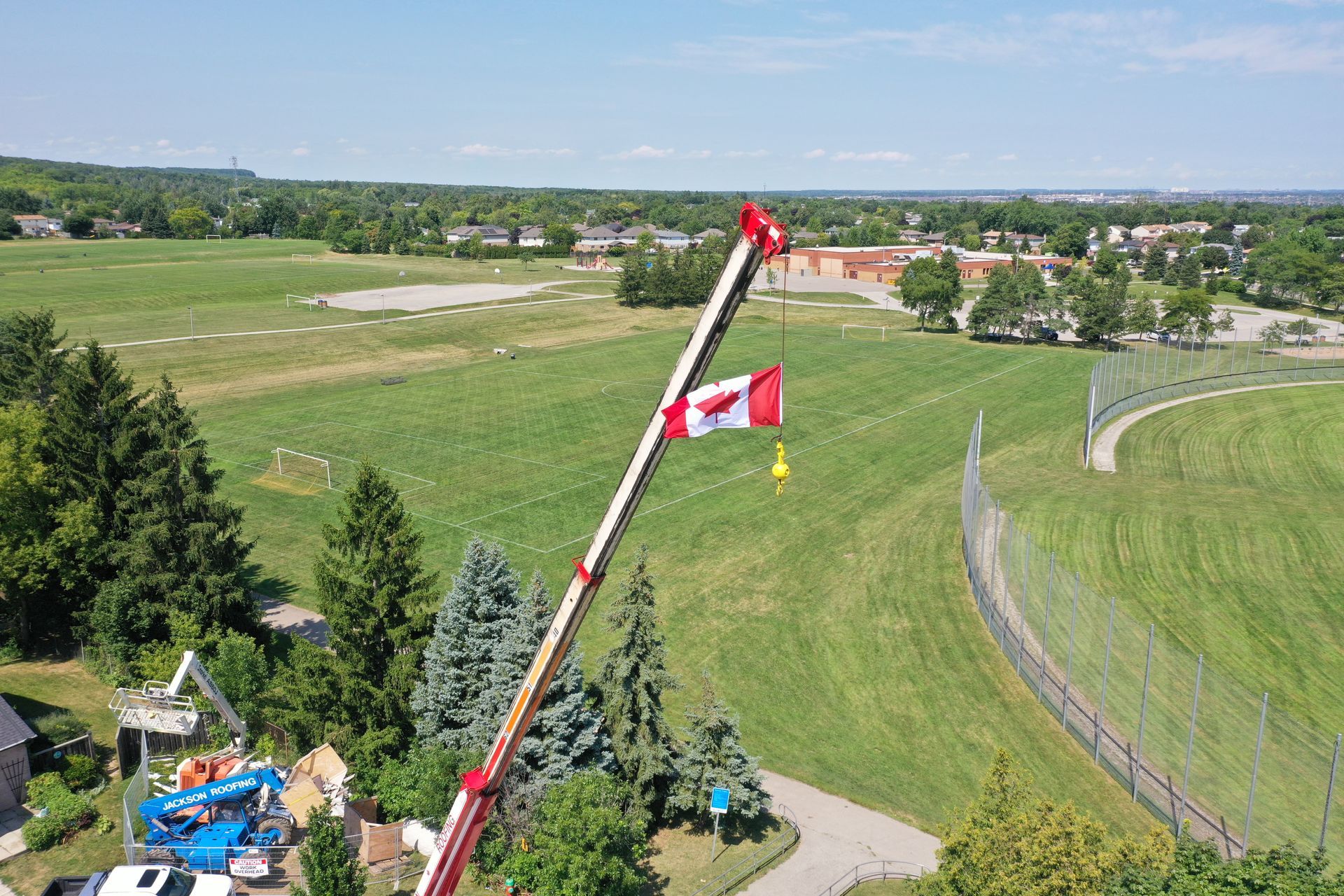An aerial view of a crane lifting a canadian flag in a field.