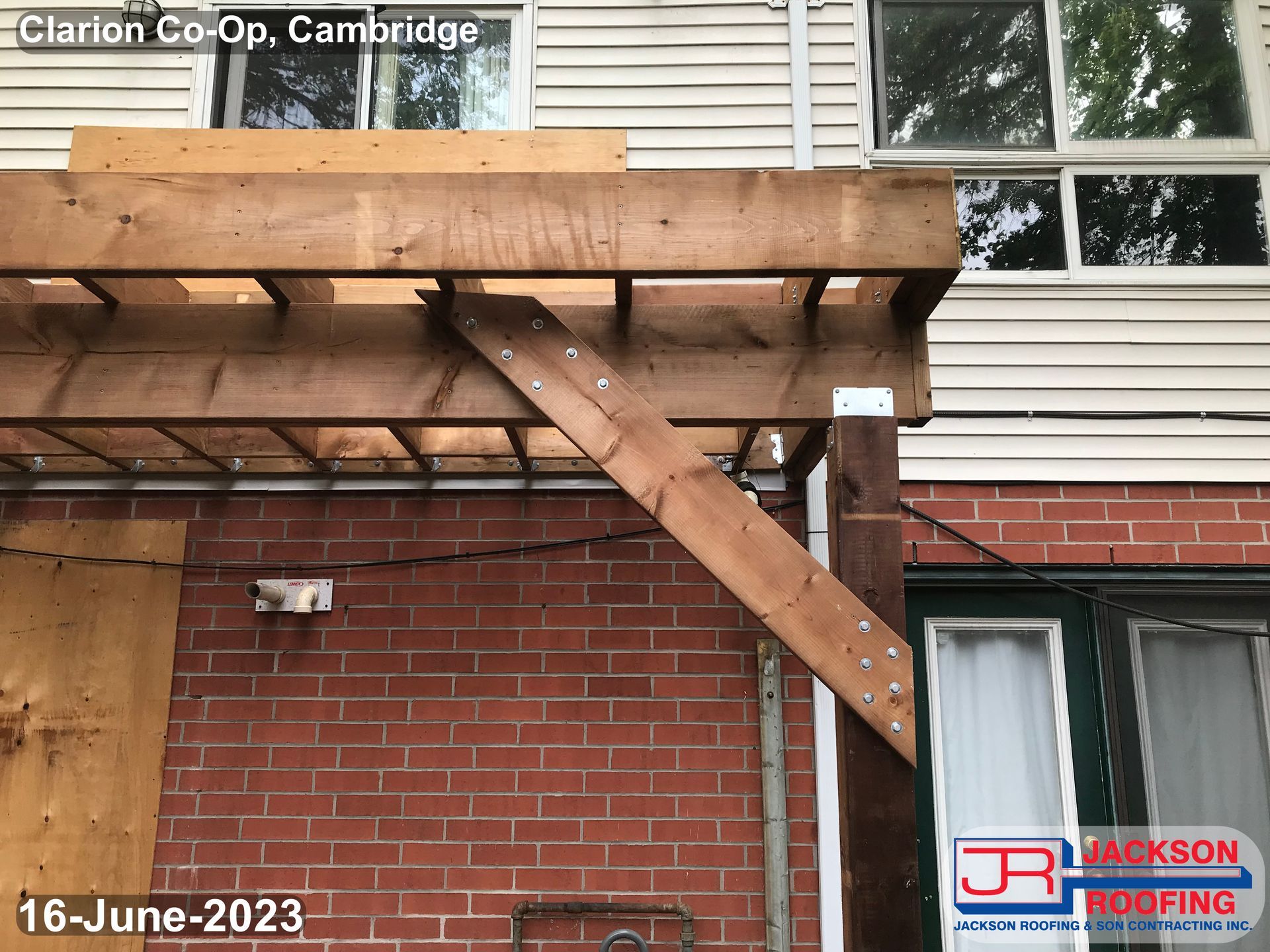 A wooden pergola is being built on the side of a brick building
