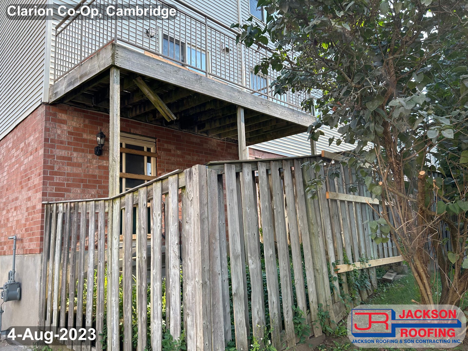 A wooden deck is being built on the side of a house next to a wooden fence.