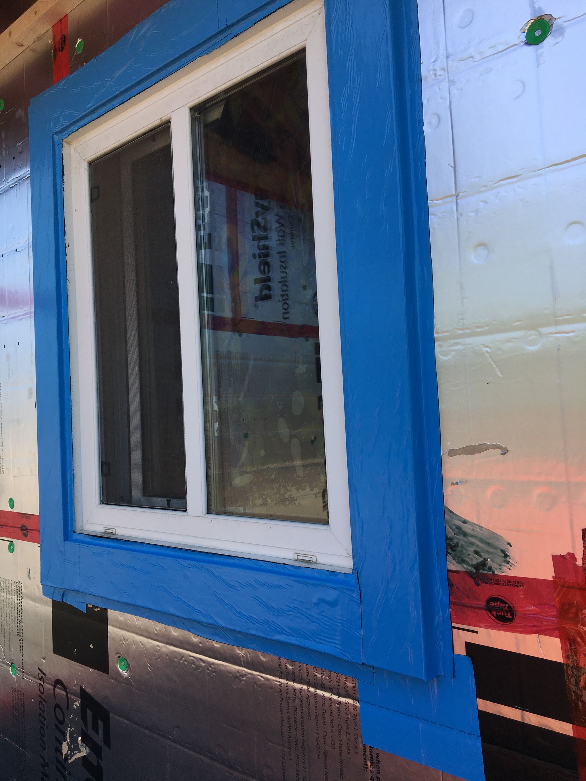 A window with a blue frame is on the side of a building.