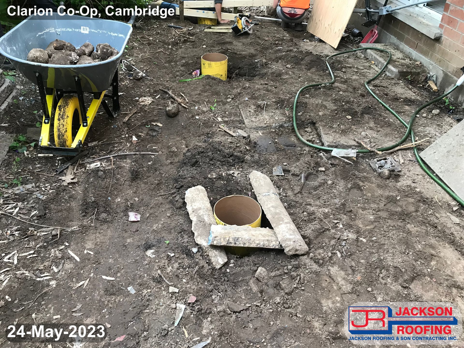 A wheelbarrow filled with rocks is sitting in the dirt next to a hose.