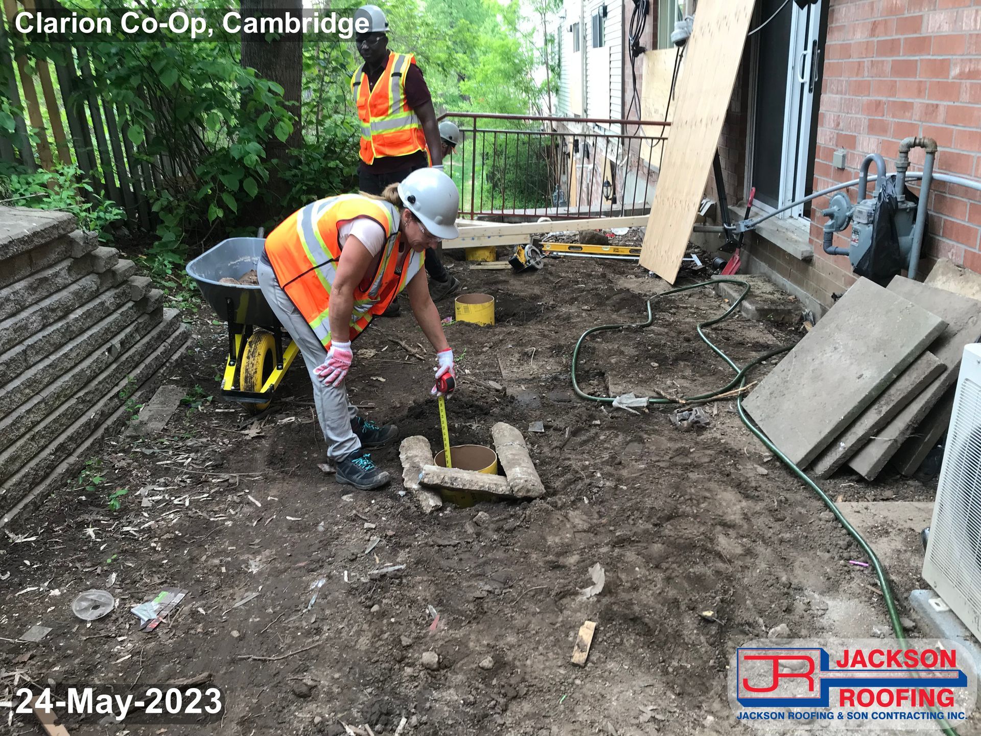 A construction worker is measuring a hole in the ground.