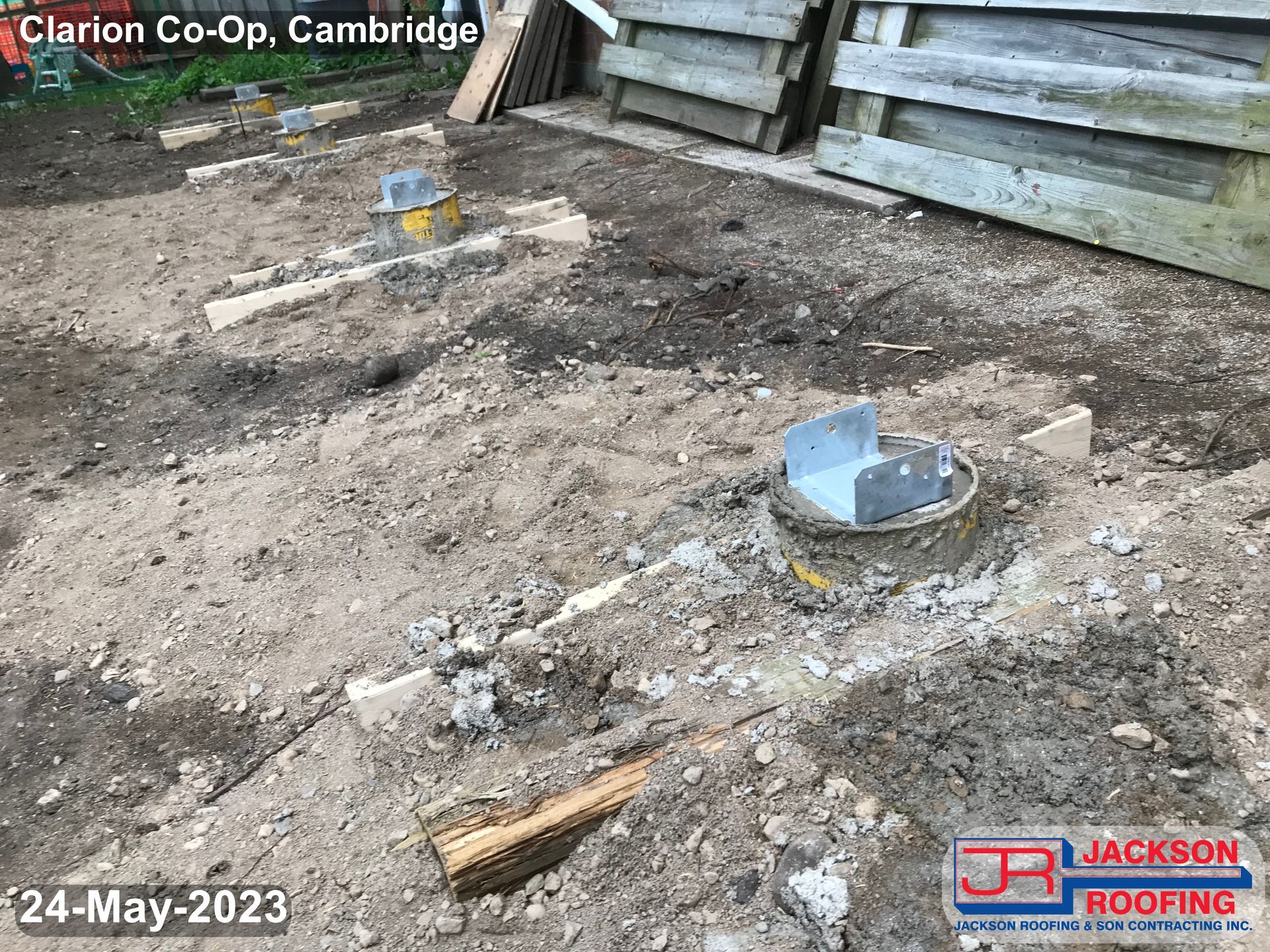 A bucket is sitting in the dirt next to a wooden fence.