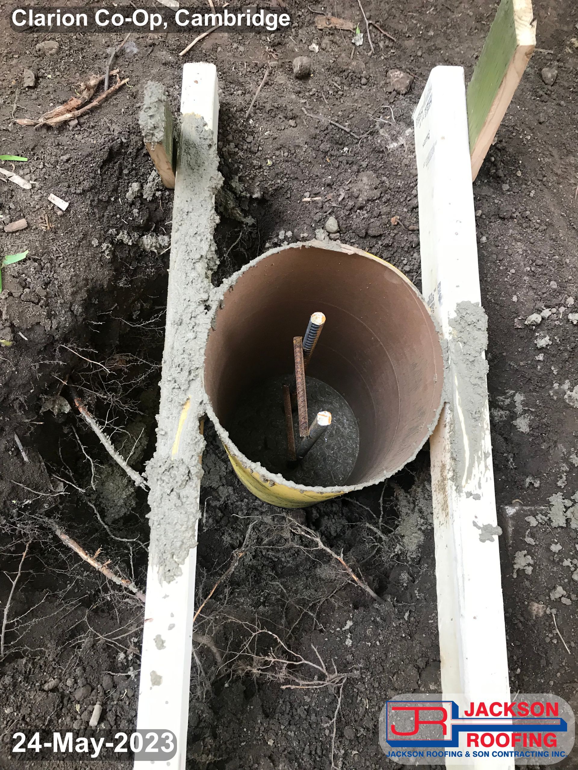 A pipe is sitting in the dirt next to a wooden post.