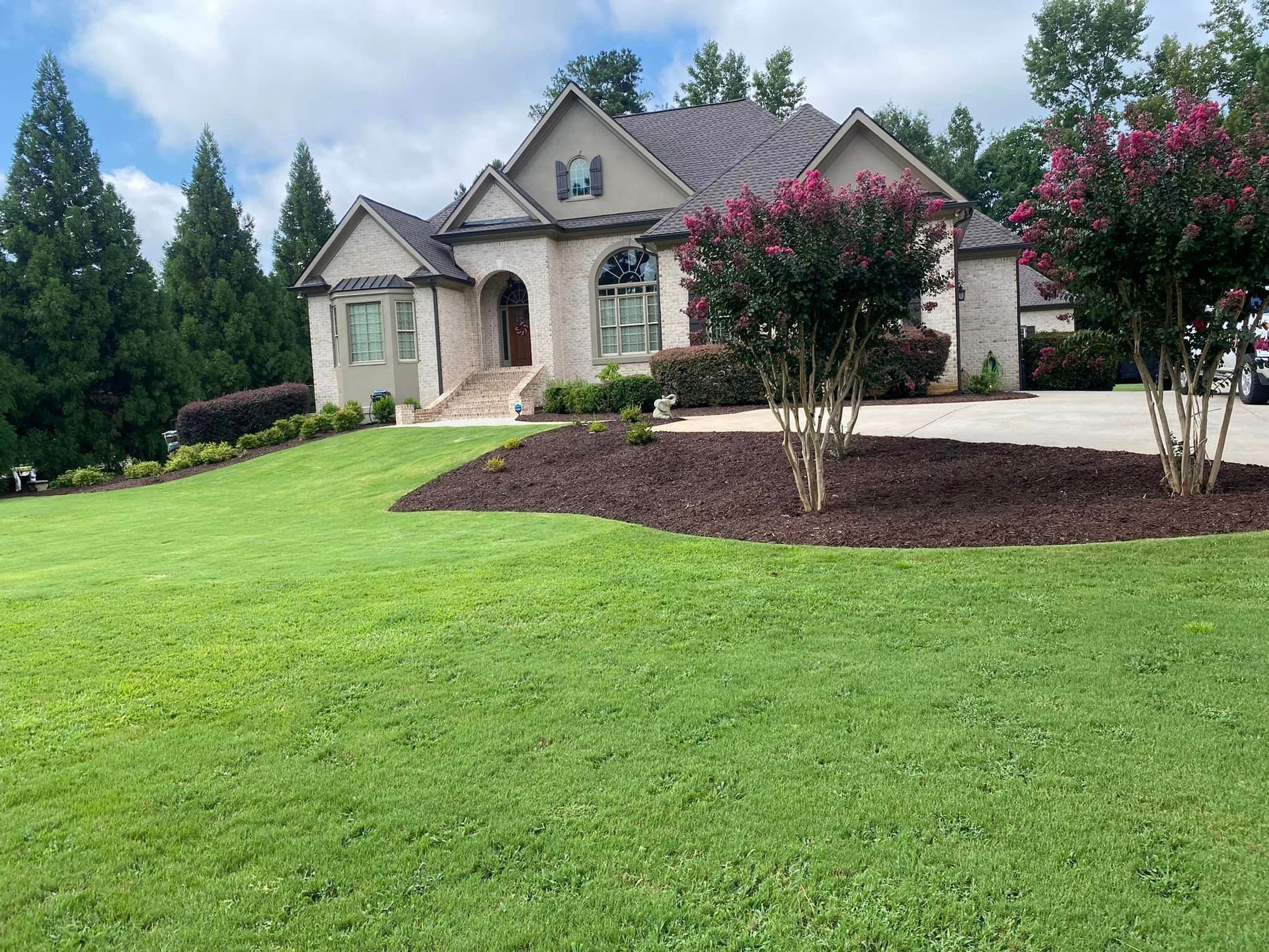 A brick house with a manicured lawn and landscaping. Pink flowers in front.