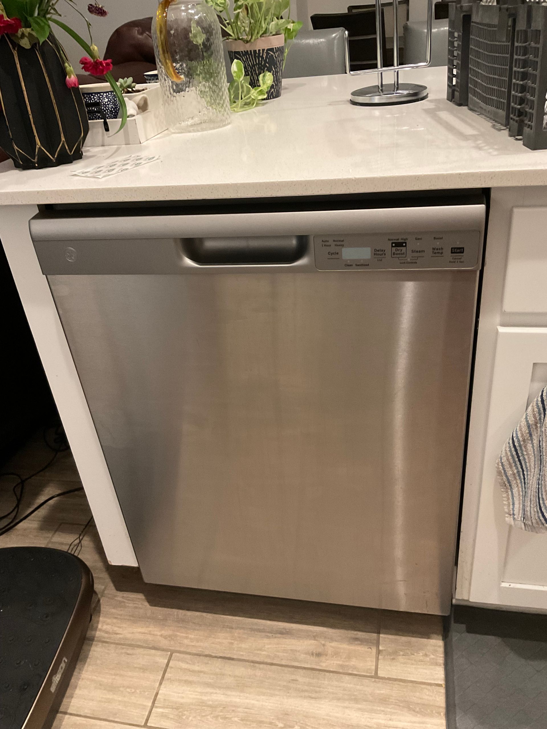 Stainless steel dishwasher under a white countertop in a kitchen.