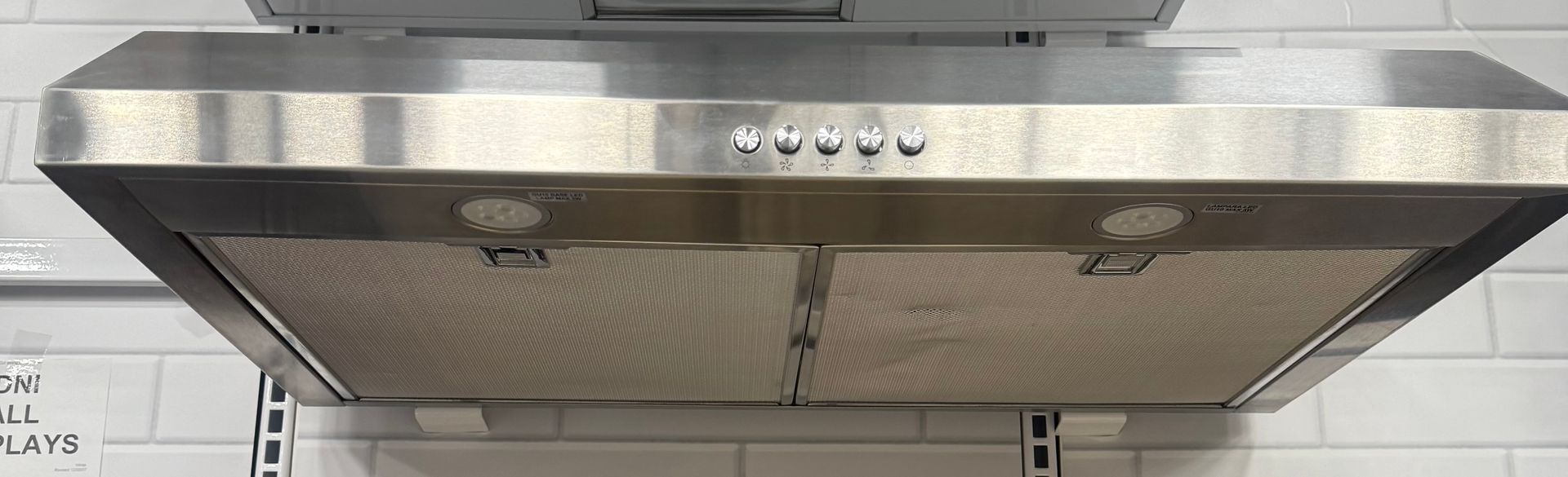 Stainless steel range hood above a white tiled backsplash.