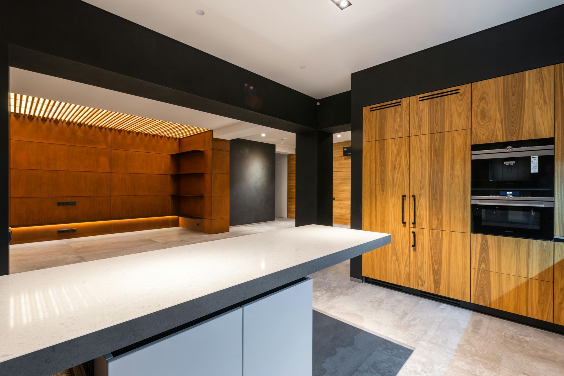 Modern kitchen with wood cabinets, white island, and dark ceiling.