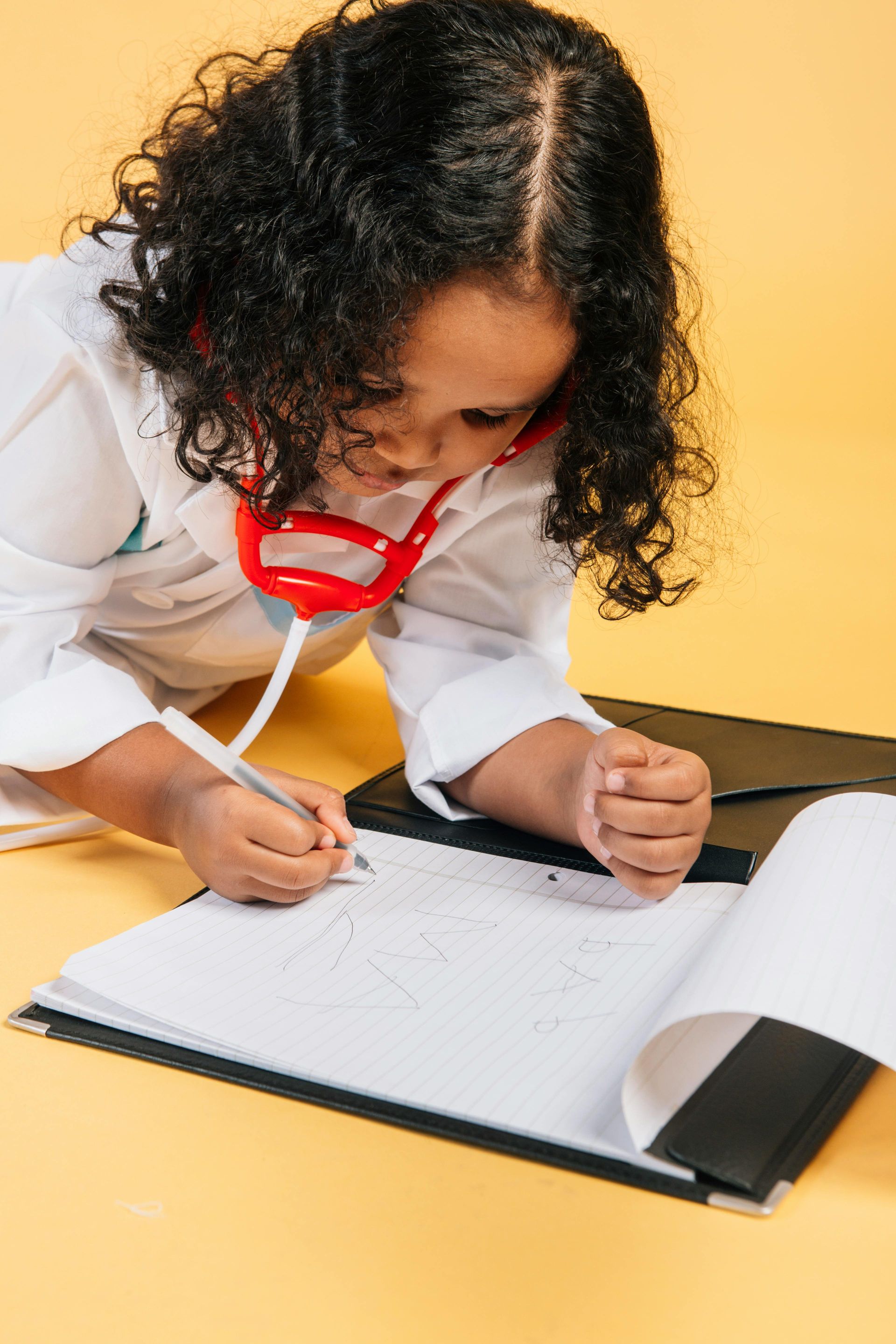 A little girl dressed as a doctor is writing in a notebook.