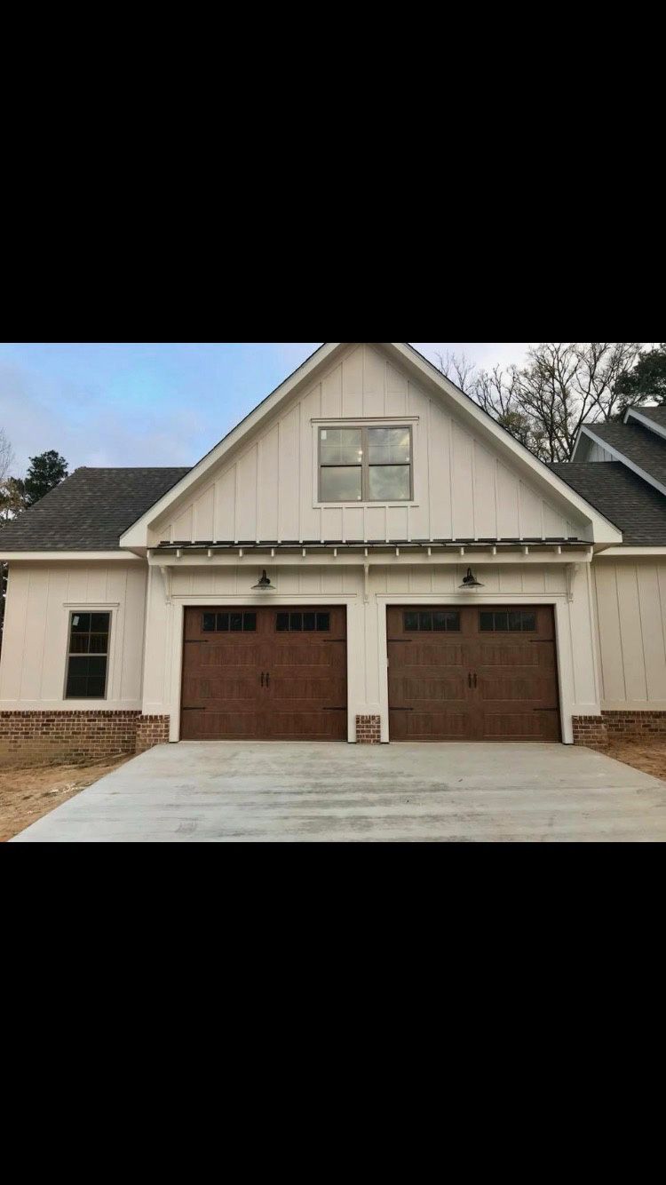 A new house with a two-car garage, brown doors, white siding, and a concrete driveway.