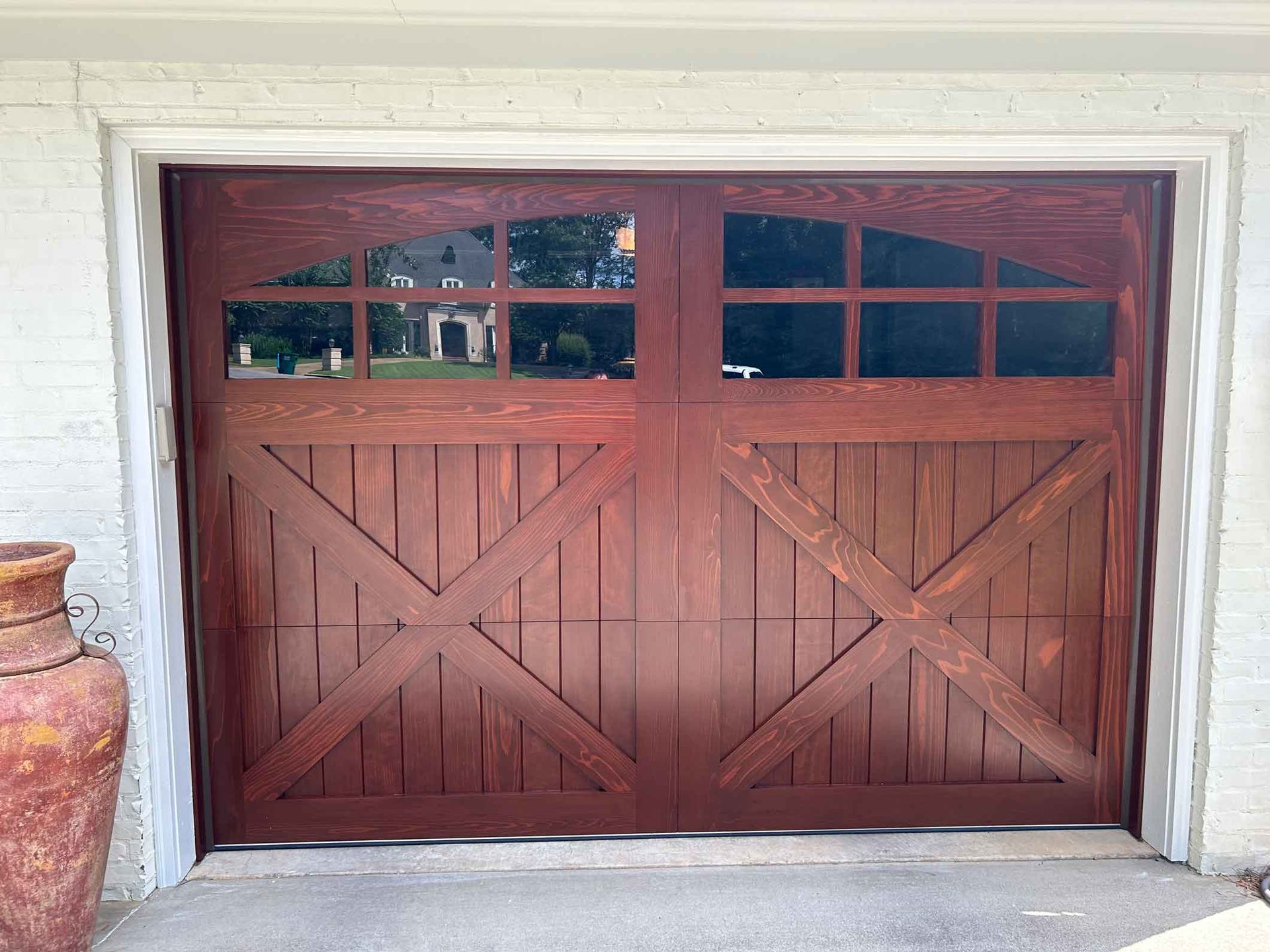 Brown wooden garage door with glass panels and an arched top, set in a white-framed opening.