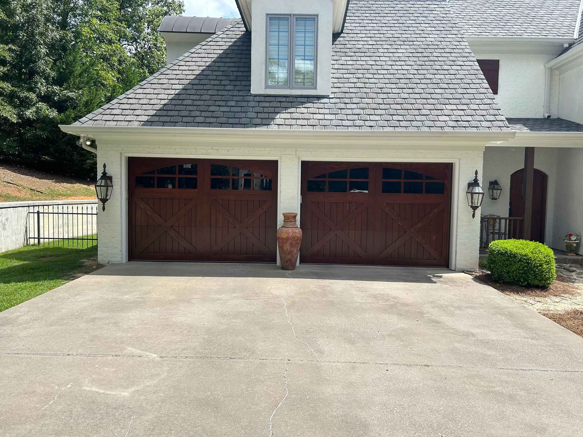 Two-car garage with brown doors, stone facade, and gray roof. Urn sits between garage doors on concrete driveway.