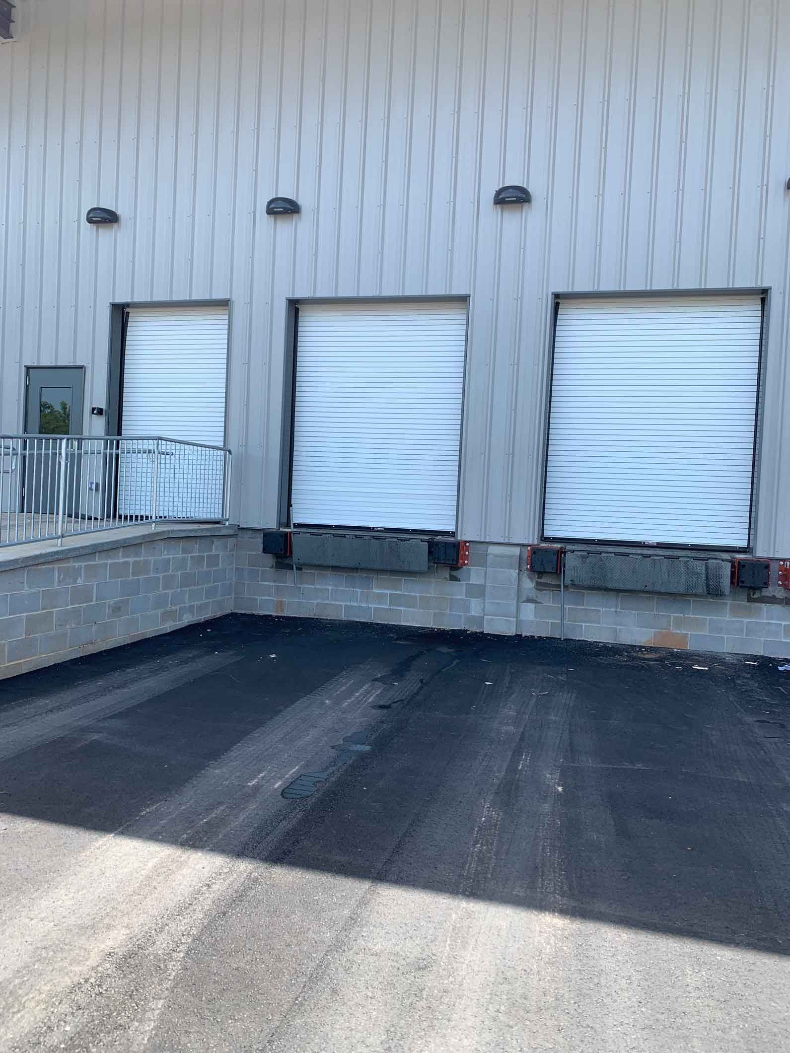 Exterior of a commercial building with three loading dock doors and a paved area.