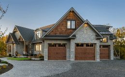 Stone house with brown garage doors and a paved driveway under a blue sky.