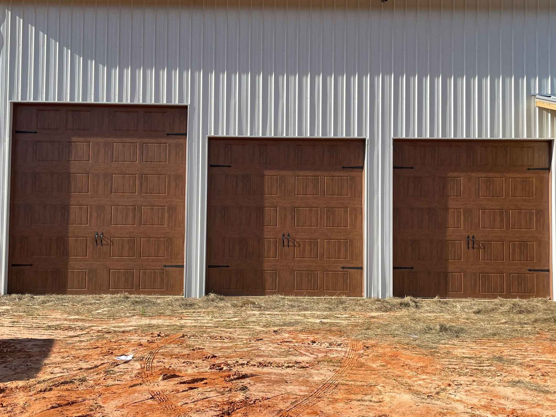 Three brown garage doors in a row against a corrugated metal building.