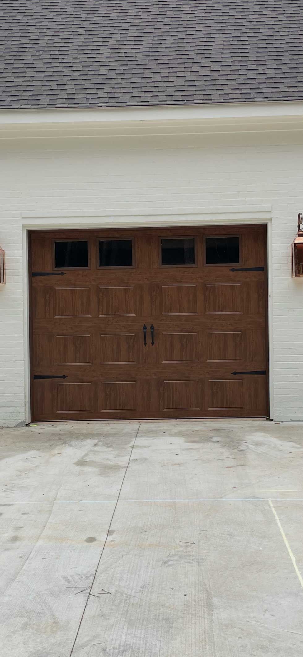 Brown garage door in a white brick building with a concrete driveway.