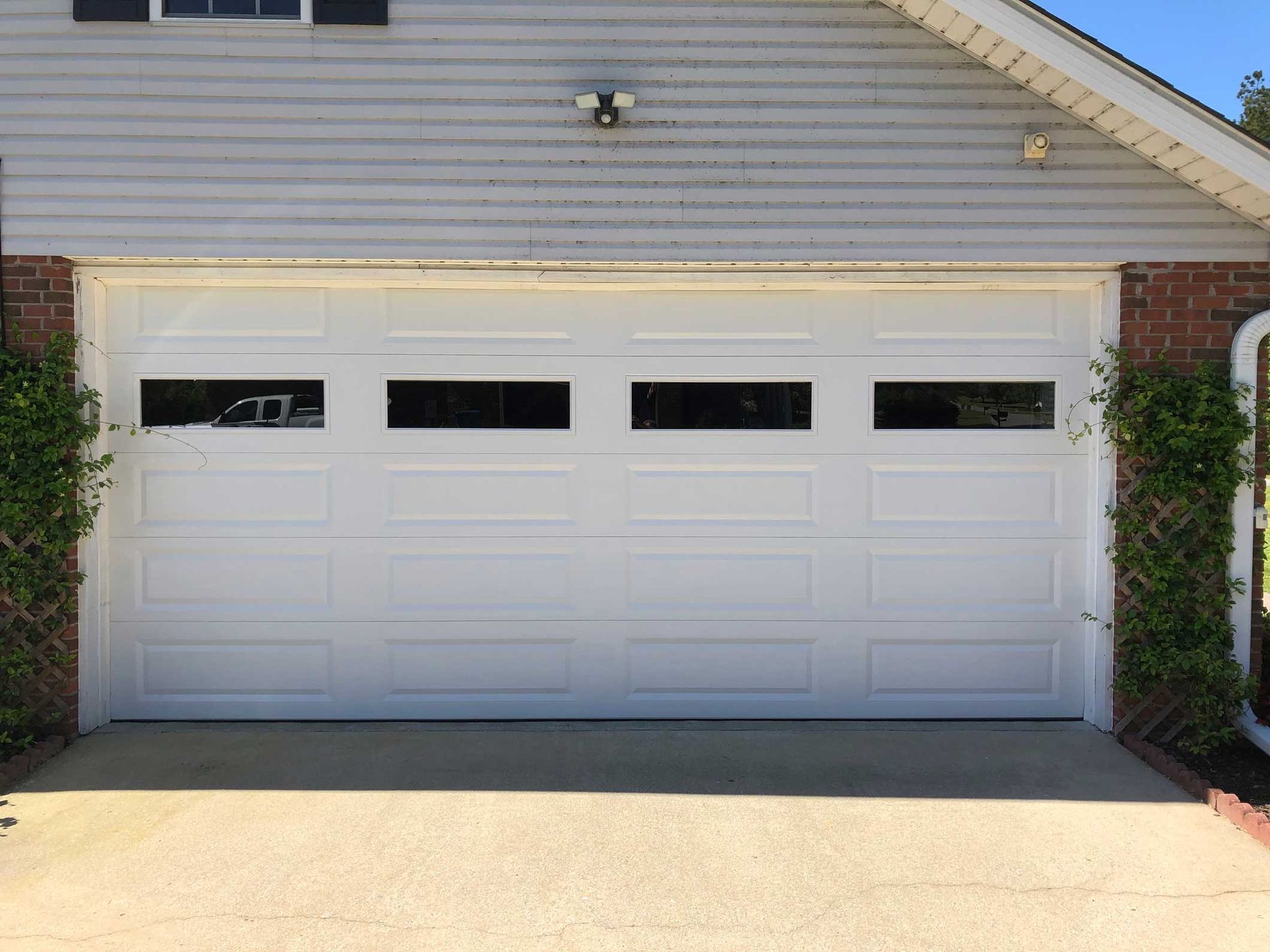 White garage door with four rectangular windows above panels on a concrete driveway.