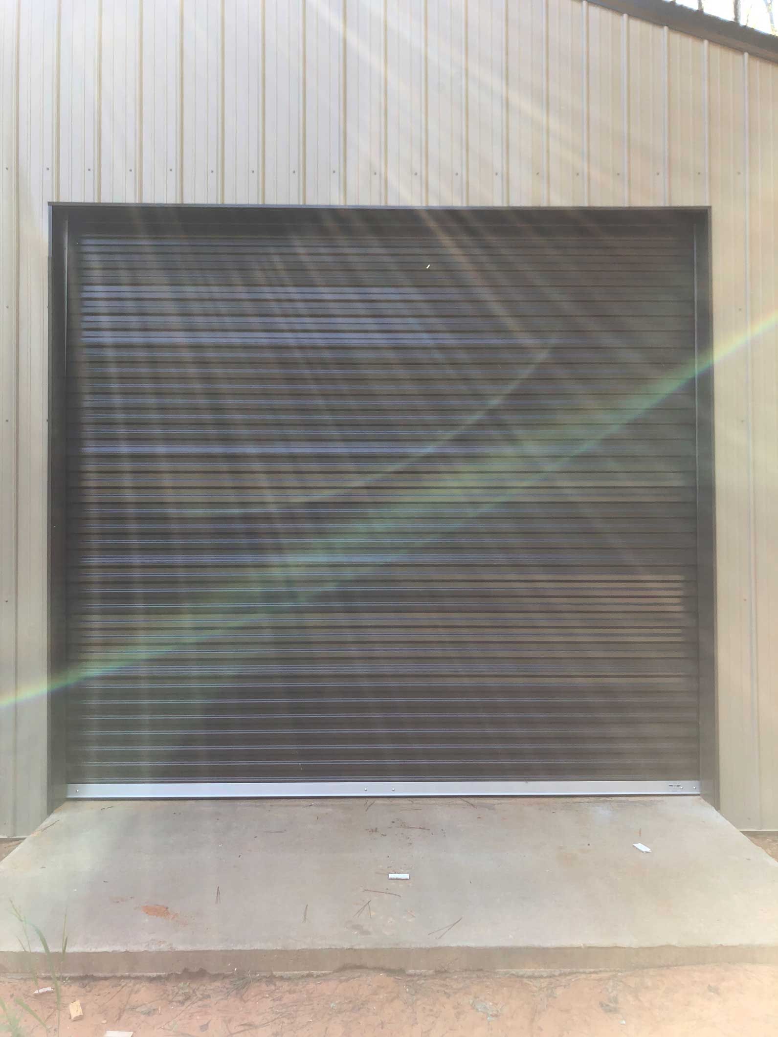 Metal roller shutter door, closed, on a concrete pad. Light-colored building with vertical panels.