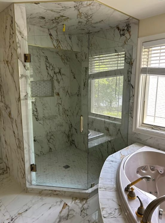 Marble bathroom with glass shower, window light, and a white soaking tub in the foreground