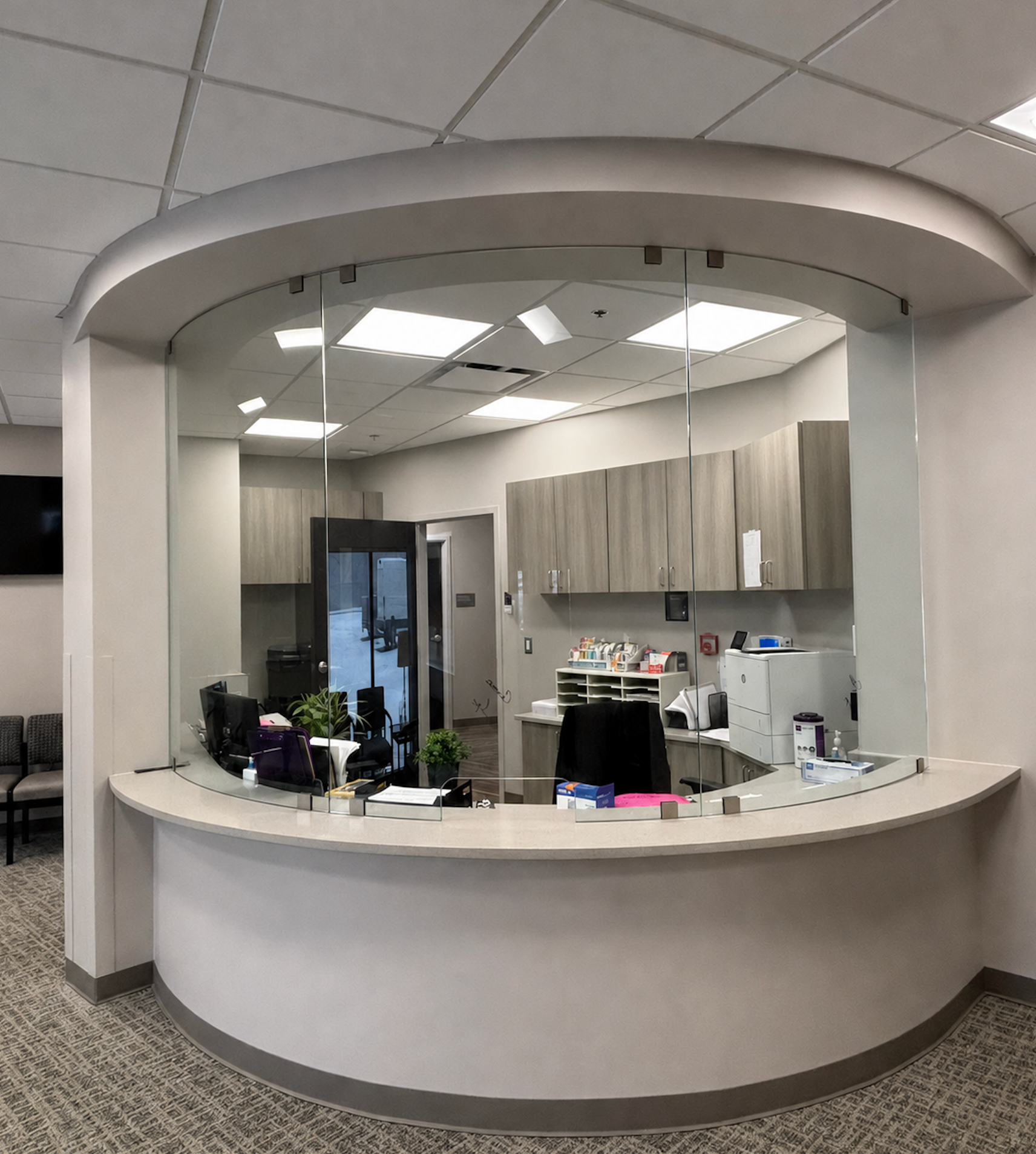 Curved white reception desk in a modern office lobby with cabinets and a glass entryway behind it
