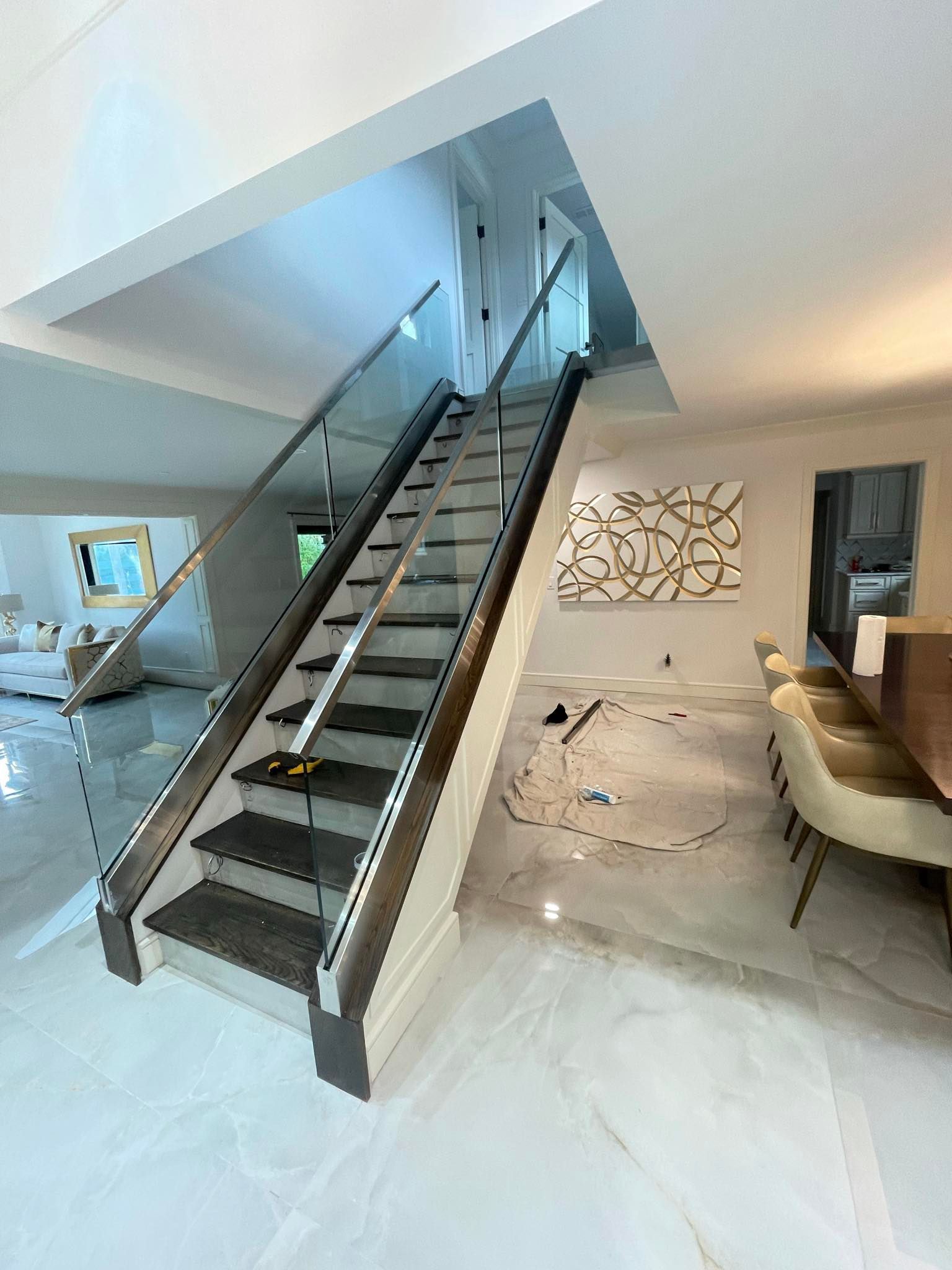 Modern living room with floating staircase, beige sofa, and marble floor under a lofted ceiling